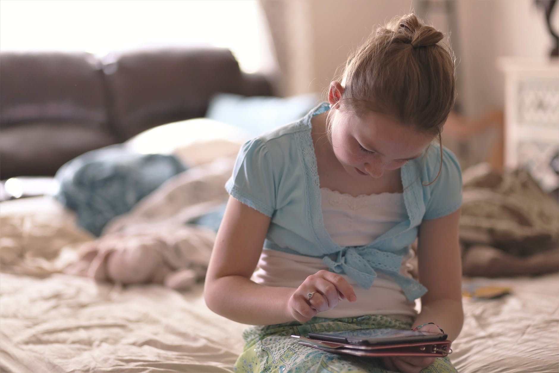 girl sitting on bed holding tablet computer