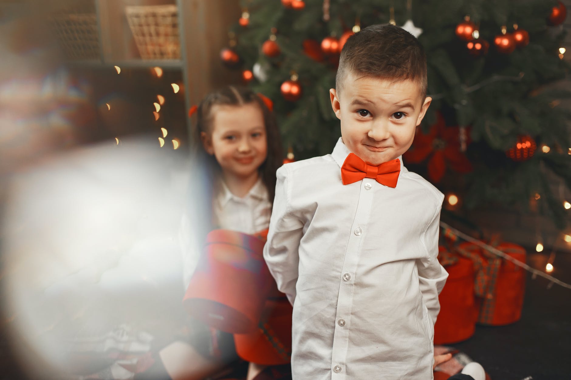 girl with a boy with a red black tie and white shirt standing by a christmas tree with red baubles