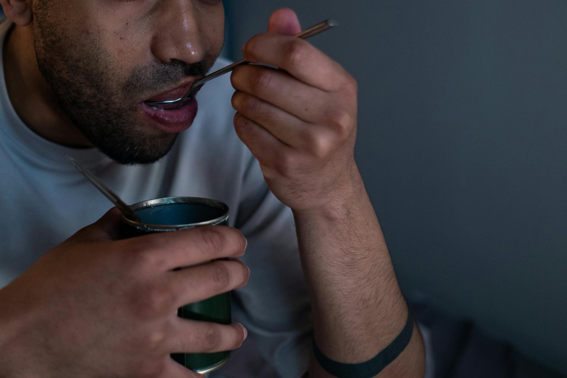 man holding silver spoon eating from the can